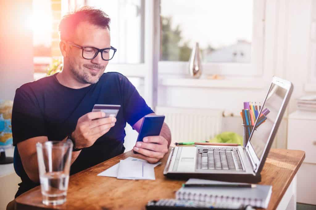 Mann mit Brille sitzt am Tisch und bezahlt online